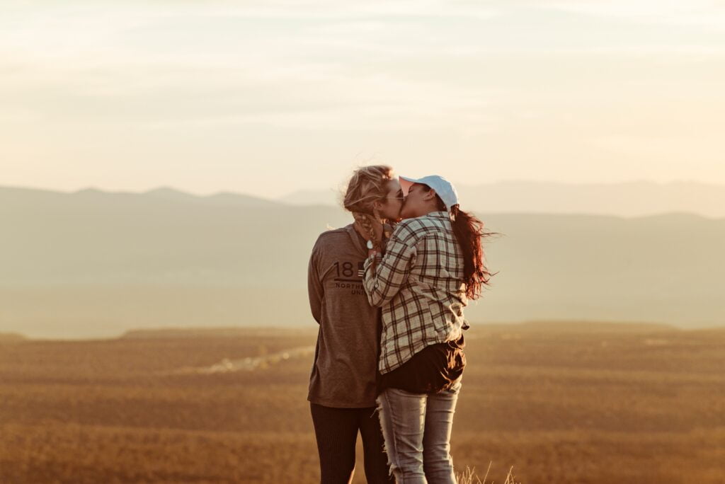 coppia di donne di baciano in un campo con colline alle spalle turismo lgbt